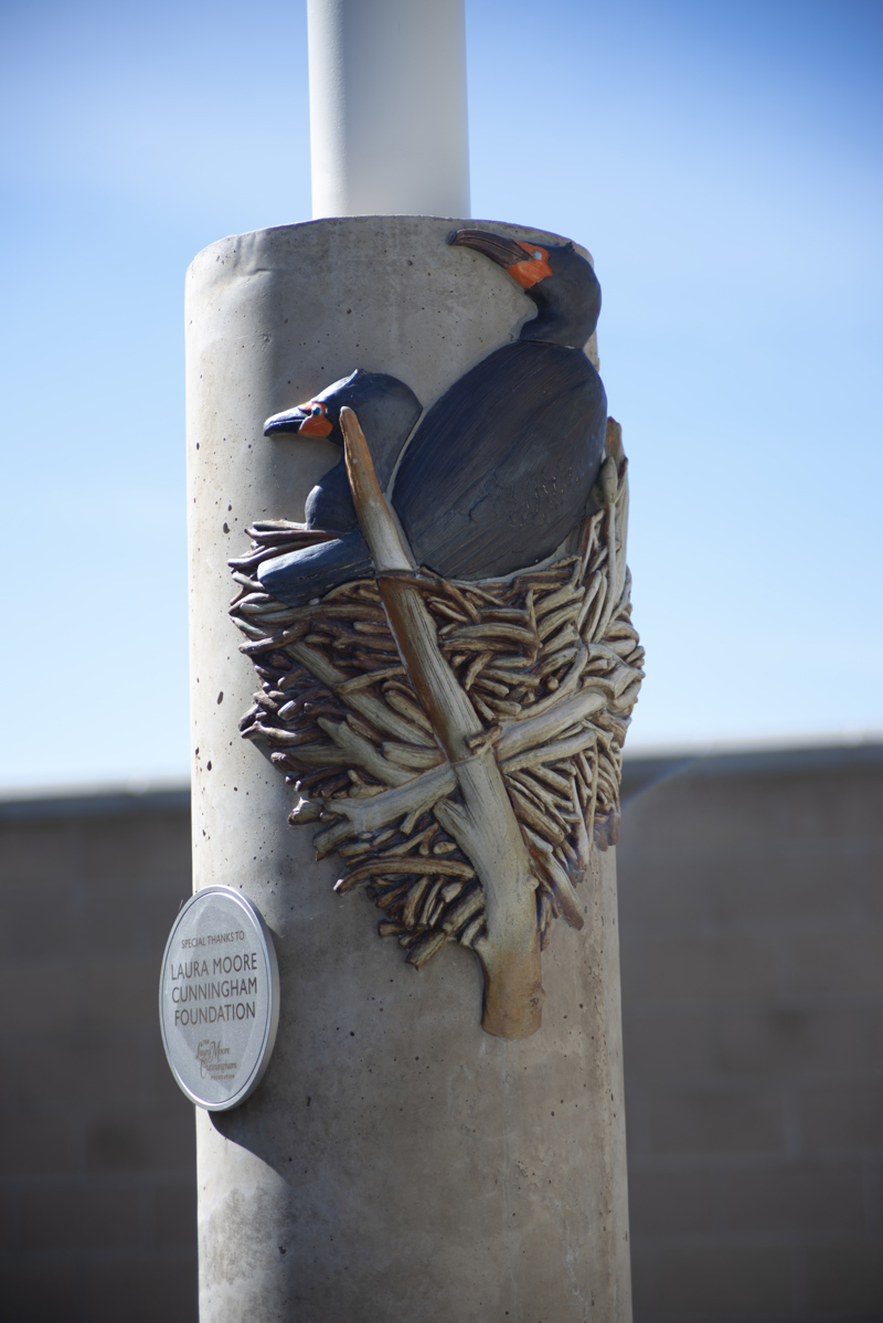 A cement column decorated with ceramic mosaic relief sculpture of a nesting pair double-crested cormorants.