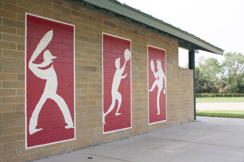 A series of three murals painted on a brick wall. Each mural depicts and abstracted figure playing baseball including a batter, a fielder, and a pitcher.