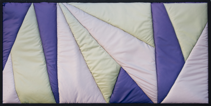 A quilted geometric abstract piece made up of blue, green, and pink textile.