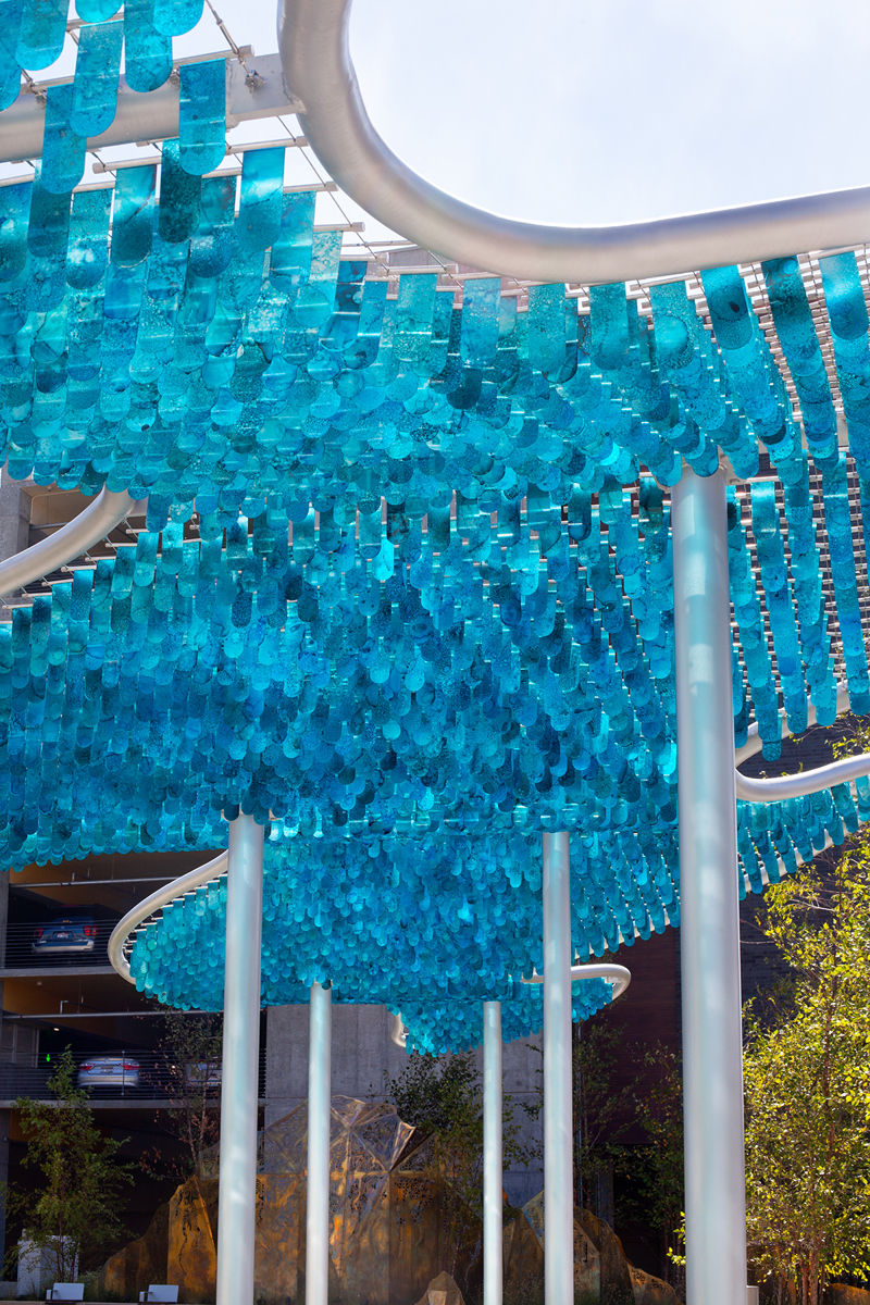 A shade canopy structure consisting of blue, alcohol painted flappers suspended in spanners set between stretched steel cables.