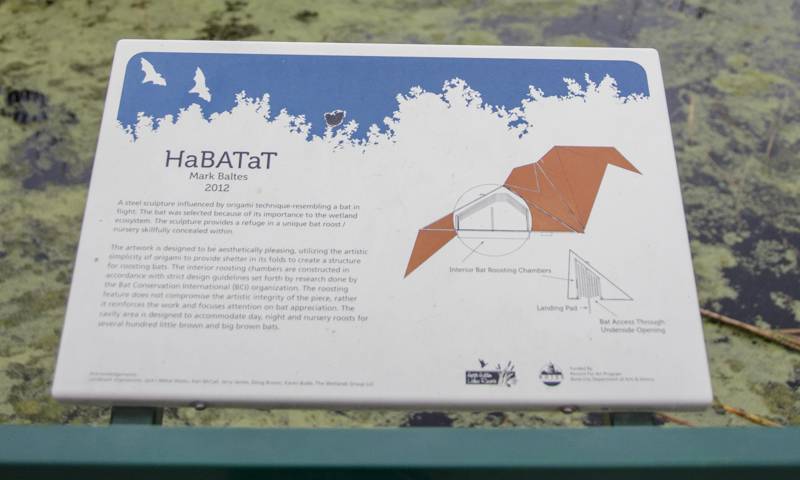 The plaque signage for the sculpture HaBATat, explaining the artist's intent that the artwork resembles an origami bat in flight, and how the sculpture serves as a bat shelter.