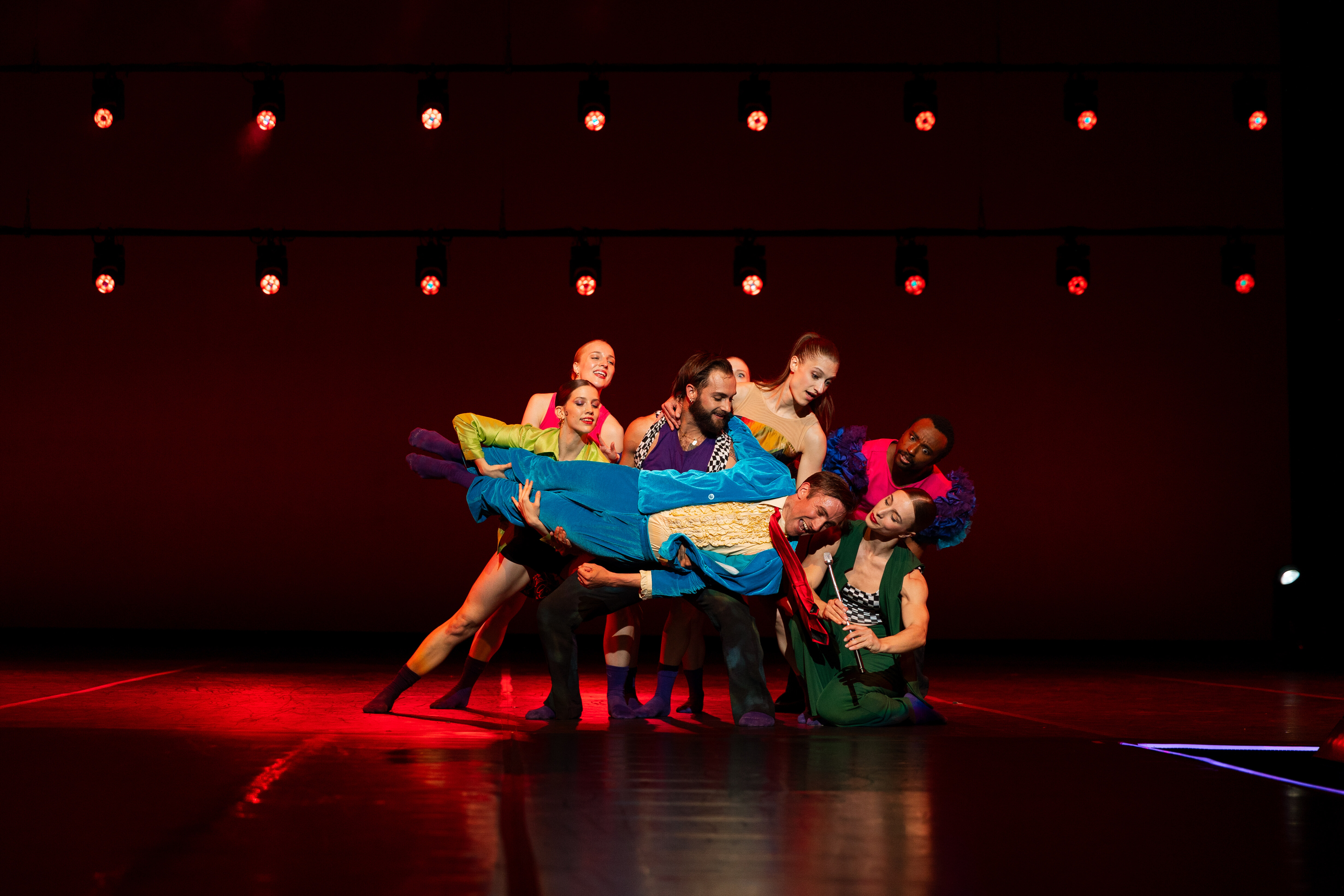 Group of performers on stage holding one performer horizontally.