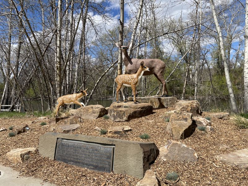 A painted sculpture of a deer and two fawns standing on a hill of rocks. Beneath them is a bronze plaque.