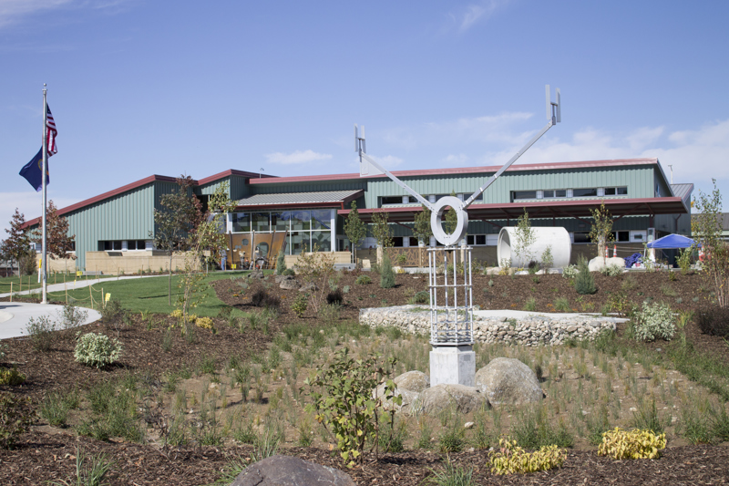 An aluminum kinetic sculpture representing a water molecule. At its central axis point is the letter O from which stems two arms with the letter H at their end. This sculpture turns in the wind like a weather vane and sits atop a column made from a stack of aluminum plates cut in the shape of snowflakes. 