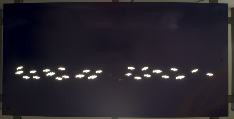 A doorway awning made of painted cut metal. In the awning, lit with backlighting, are holes in the shape of fish.