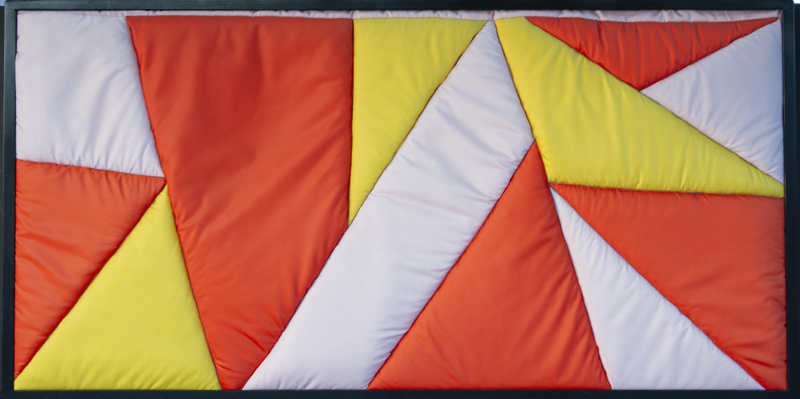 A quilted geometric abstract pieces made up of orange, yellow, and white textile.