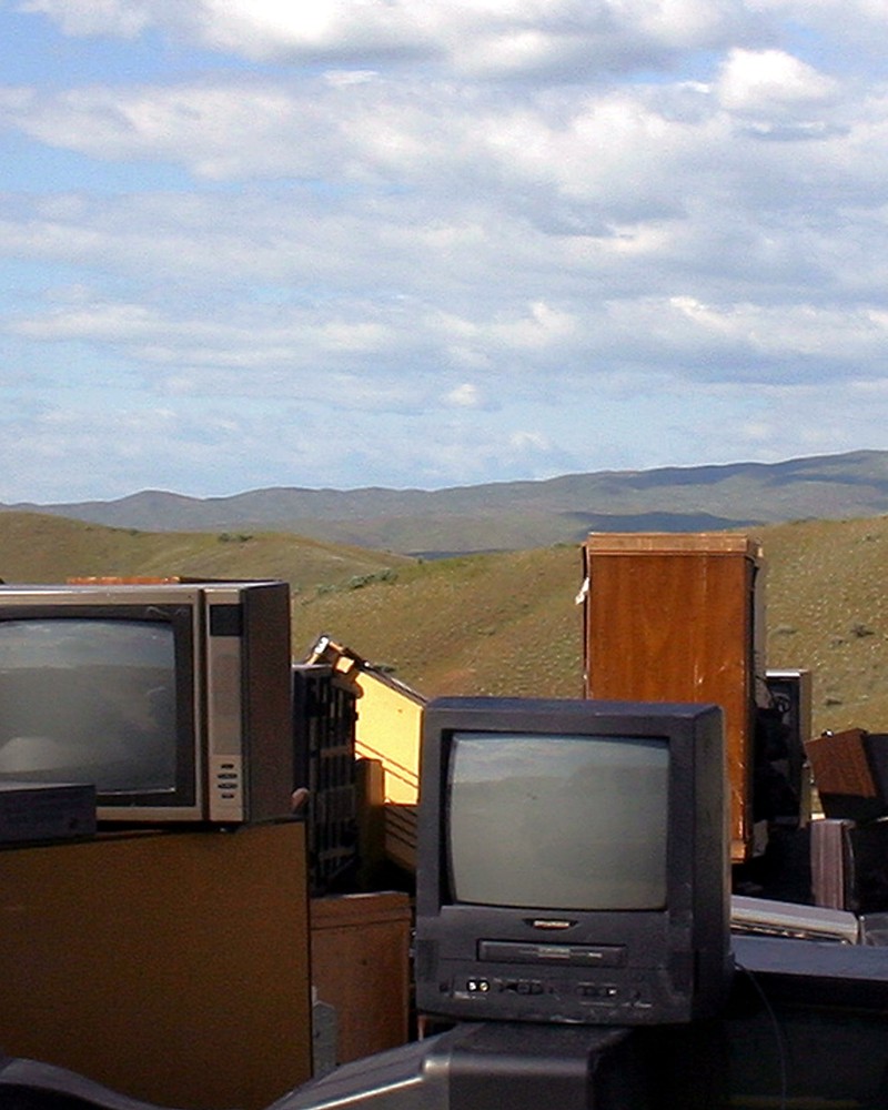 Several inactive television units piled up on a sagebrush desert landscape. 