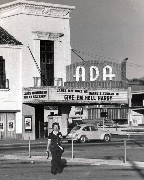 Woman walks in front of Ada Theater with sign reading James Whitmore as Harry S. Truman in Give 'Em Hell Harry.