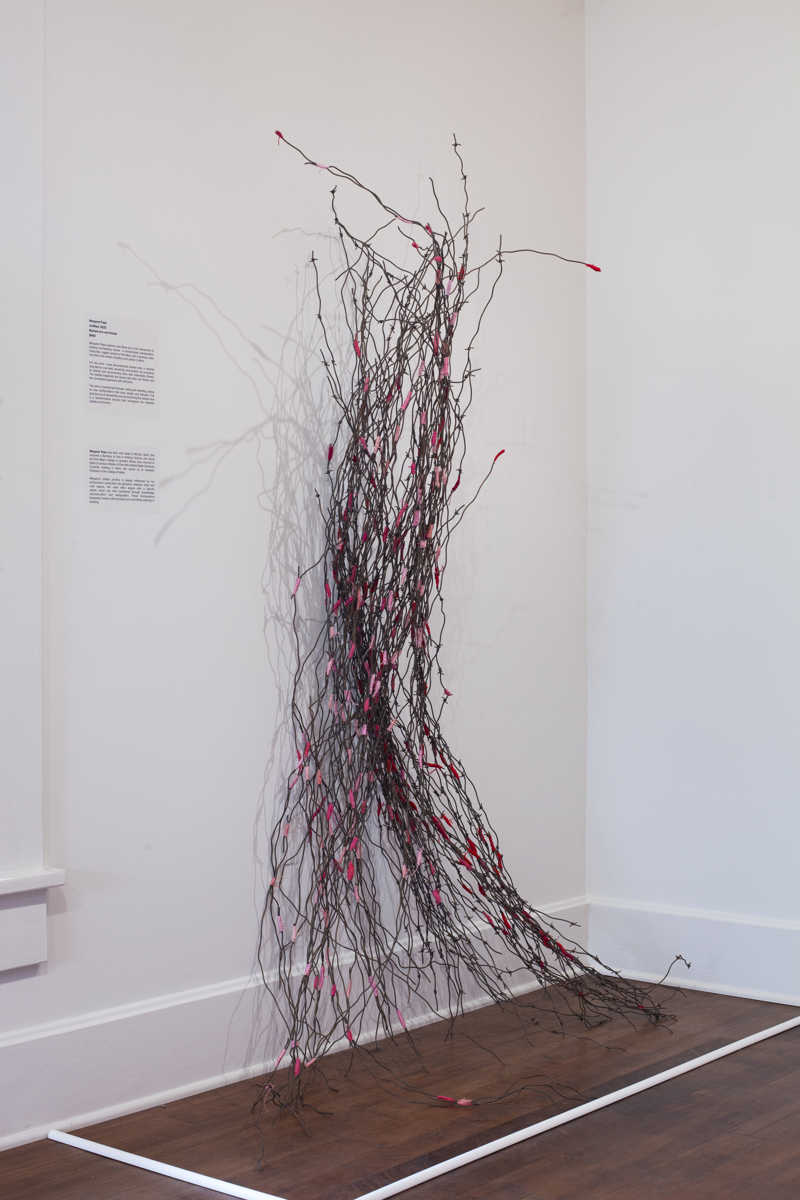 Two bundles of barbed wire, held together by pink thread, leaning up against a white wall.