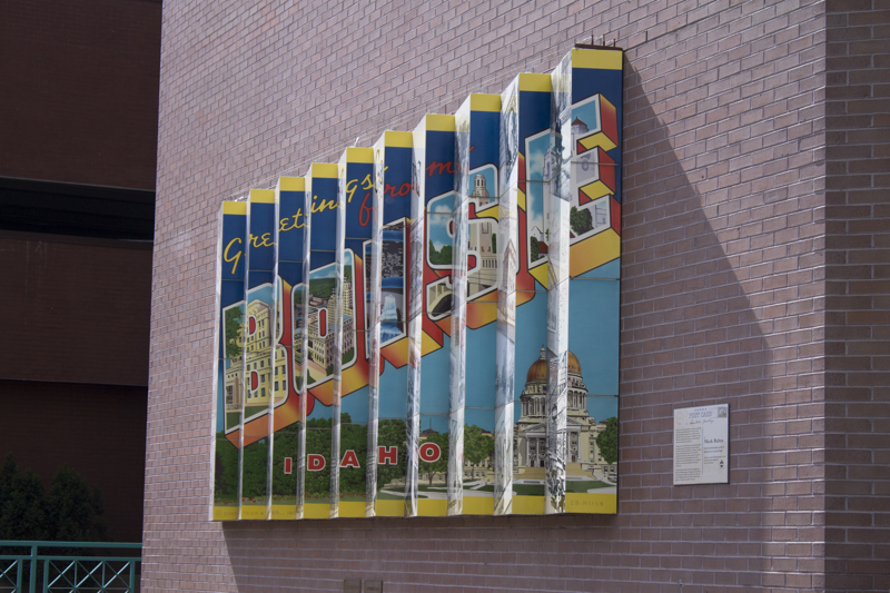 An installation of 10 rectangular layers overlapping one another like fallen dominoes. The surface of one side depicts a collection of photos a postcards of or from Boise. The other thinner edge depicts a single vintage postcard with the prominent text "BOISE". This give the illusion of seeing two different images from two different angles.