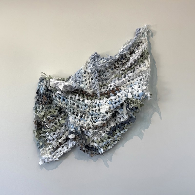 This 3-dimensional artwork is made of a variety of blue died and colored fabric pieces of silk, chiffon and polyester. Knotted together to form a gridded net like object. It organically drapes on the wall and measure approx. 34" high x 38" wide 2" deep. 