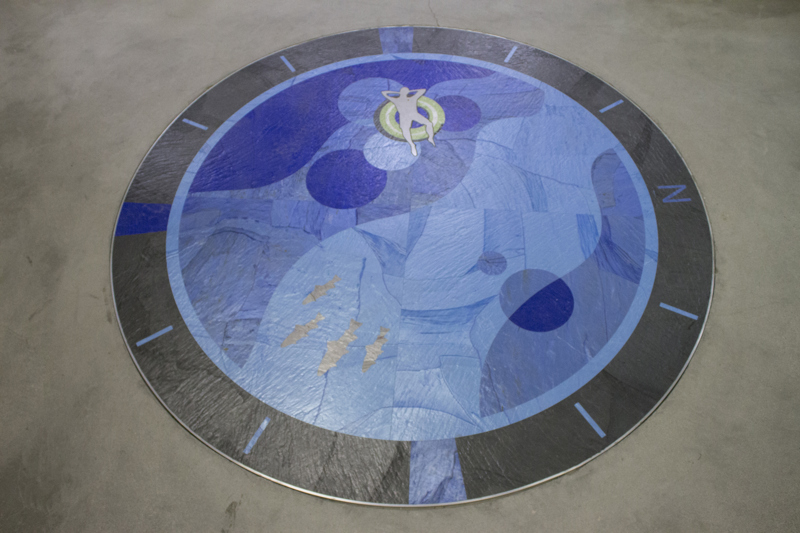 A floor inlay medallion depicting a person in an innertube floating the Boise River. Around the outside of the medallion are the cardinal directions with the letter N indicating north. 