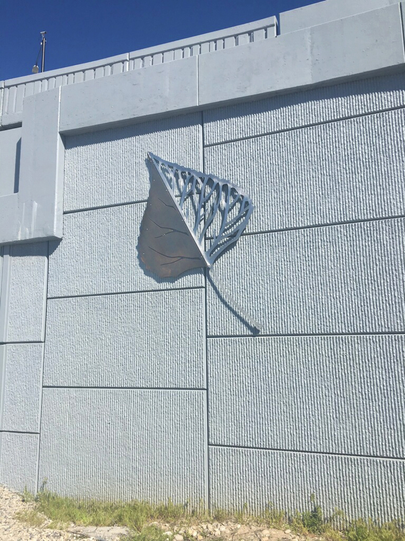 A stainless steel sculpture of a cottonwood leaf mounted to the exterior wall of a freeway overpass. 