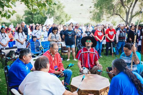 Gathering at Return of the Boise Valley People with circle of people playing a drum with onlookers in the background.