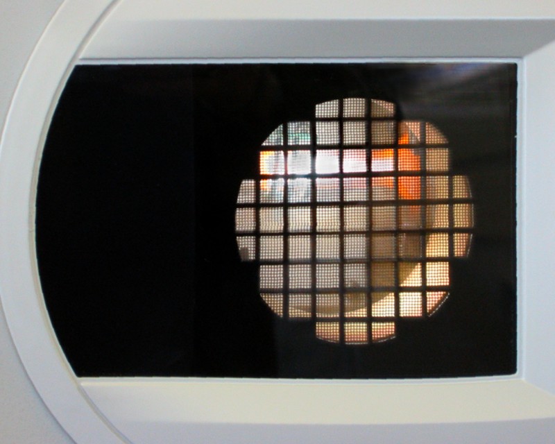 A surface resembling a microwave door with a round black grate covering a woven screen with a light emanating from behind it.  