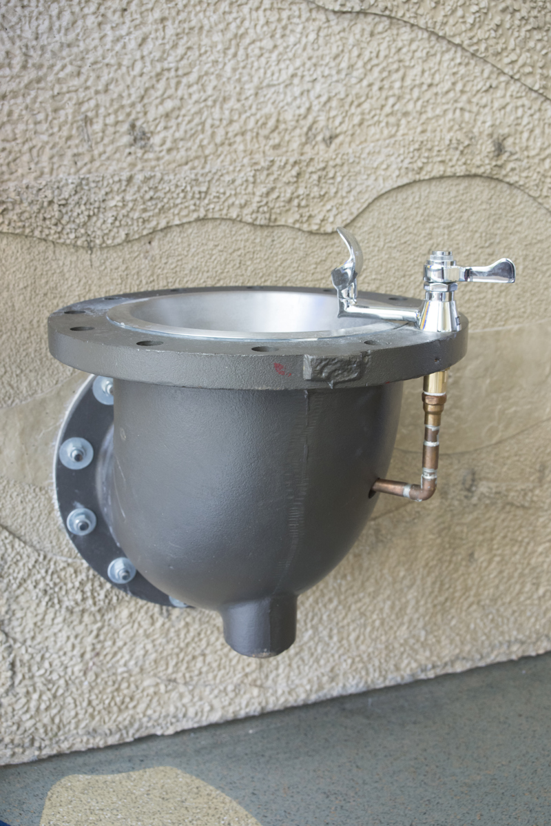 A drinking fountain made from a large metal water main L-pipe.
