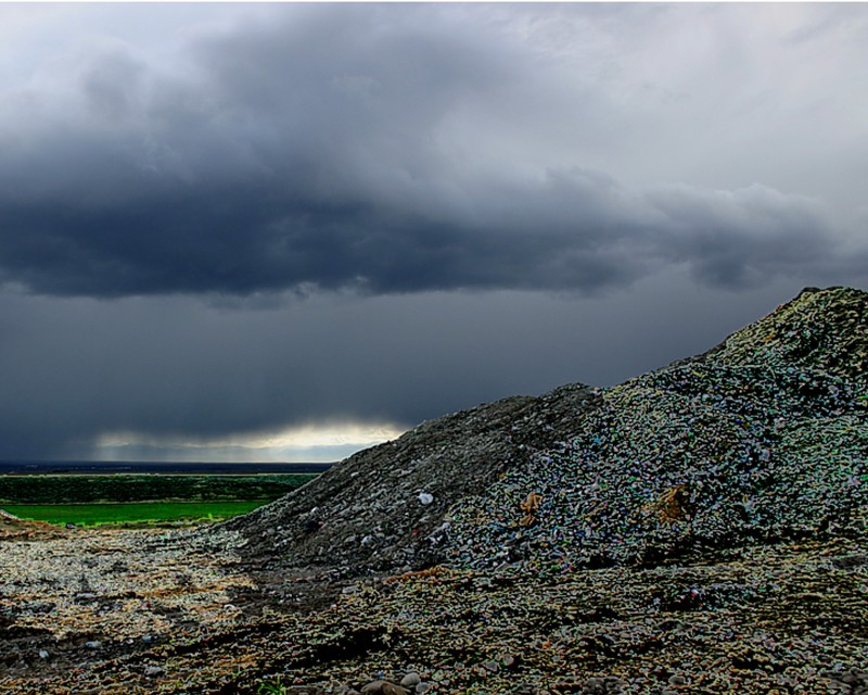 A large pile of broken glass in a field. In the background is heavy overcast of grey rain clouds. 
