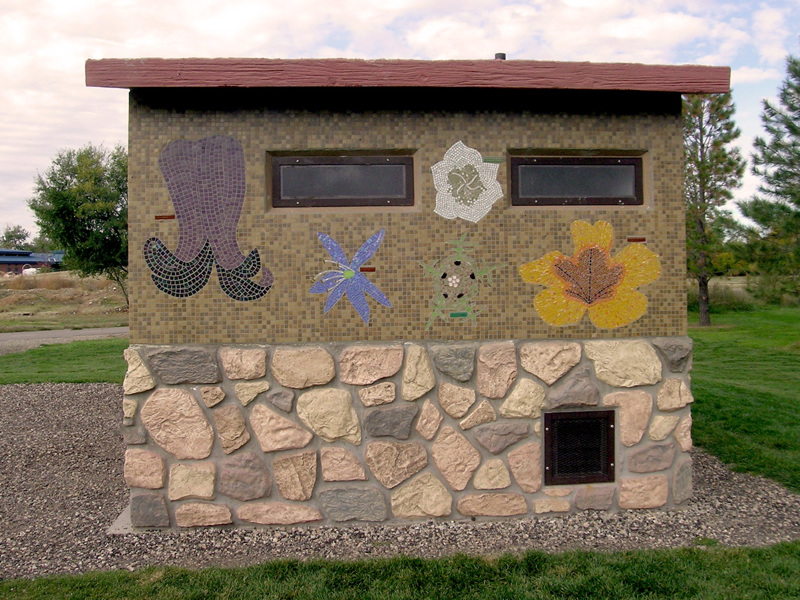 A small park bathroom building with sides covered in tile mosaics depicting flowers found in the state of Idaho. 