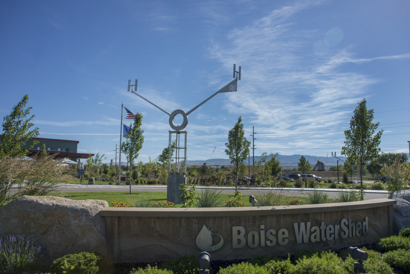 An aluminum kinetic sculpture representing a water molecule. At its central axis point is the letter O from which stems two arms with the letter H at their end. This sculpture turns in the wind like a weather vane and sits atop a column made from a stack of aluminum plates cut in the shape of snowflakes. 