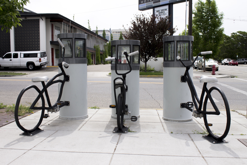 Three immobile bicycles individually attached to three cylinder structures in place of their front wheels. The tops of the cylinders have glass windows where internal musical mechanism are visible. 