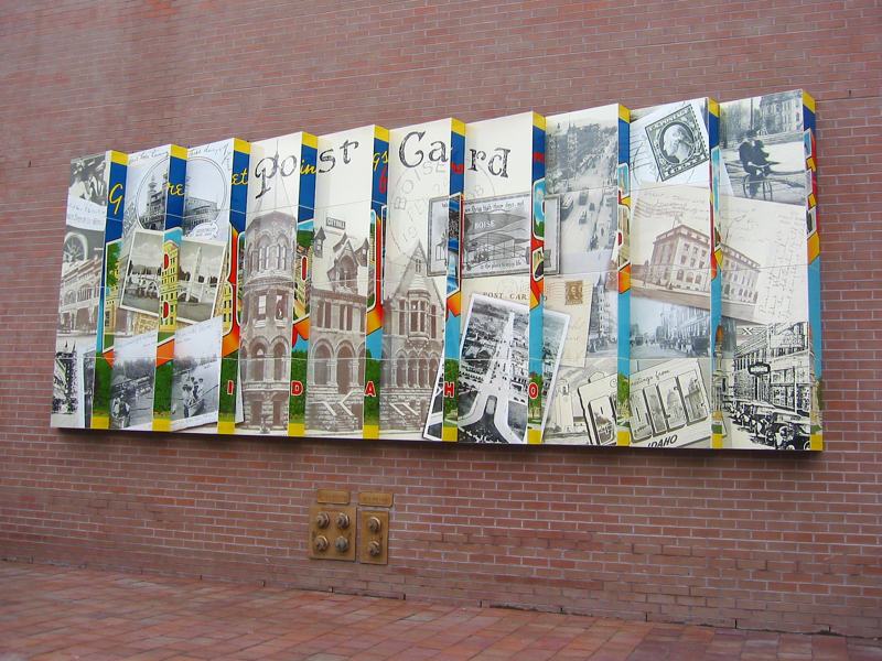 An installation of 10 rectangular layers overlapping one another like fallen dominoes. The surface of one side depicts a collection of photos a postcards of or from Boise. The other thinner edge depicts a single vintage postcard with the prominent text "BOISE". This give the illusion of seeing two different images from two different angles.