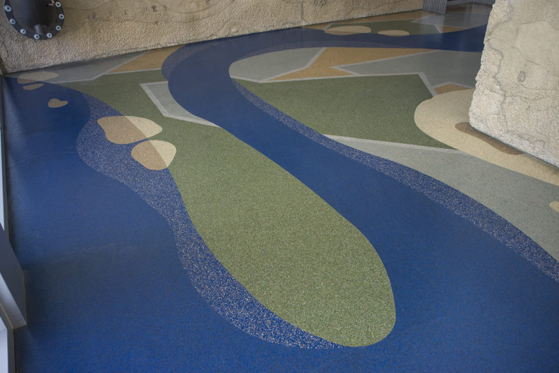 A terrazzo floor made to resemble a blue river meandering through a green landscape of green and yellow fields.