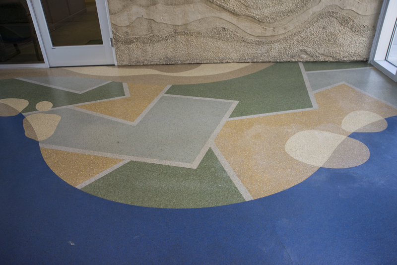 A terrazzo floor made to resemble a blue river meandering through a green landscape of green and yellow fields.