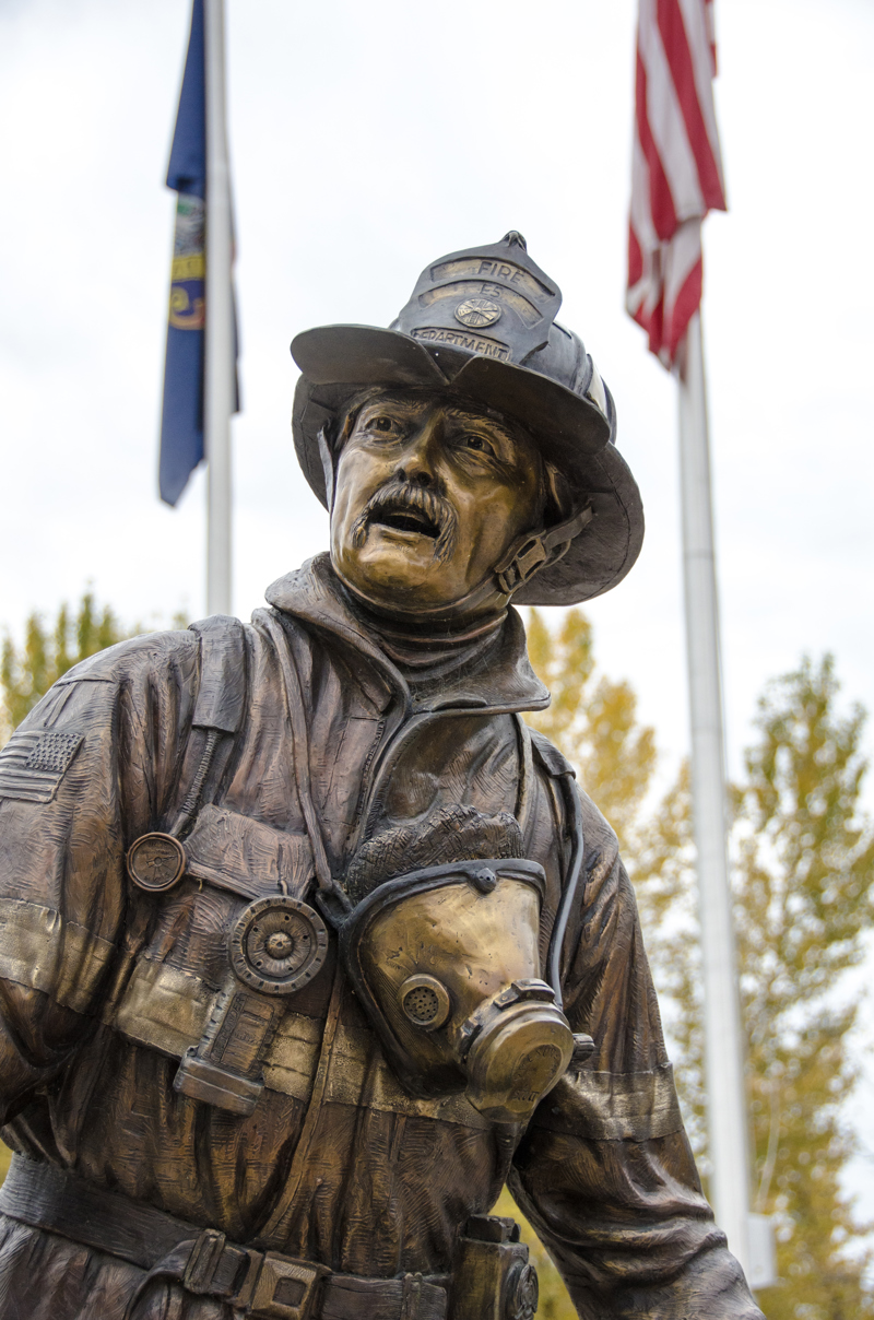 A life-sized bronze sculpture of three firefighters. One lies lifeless in the arms of another. The third stands beside them. 