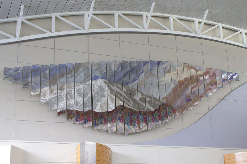A hanging installation made up of 32 quilted banners of undulating length. Their quilted pattern depicts a snowcapped mountain with flowers in the foreground.