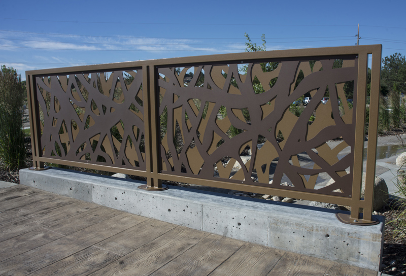 A safety railing made of two layers of brown-painted steel panels cut to resemble the tangled materials used in a beaver dam. 