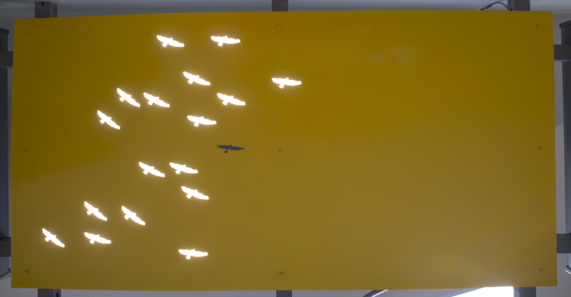 A doorway awning made of painted cut metal. In the awning, lit with backlighting, are holes in the shape of birds.