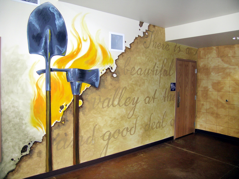 The main office of the Boise Foothills Learning Center. On the walls is painted a mural depicting flames, firefighting tools, and the fragment of some written text that reads, "There is a... beautiful... valley at the... and good deal...". On an adjacent wall is an elevation map with quadrants.