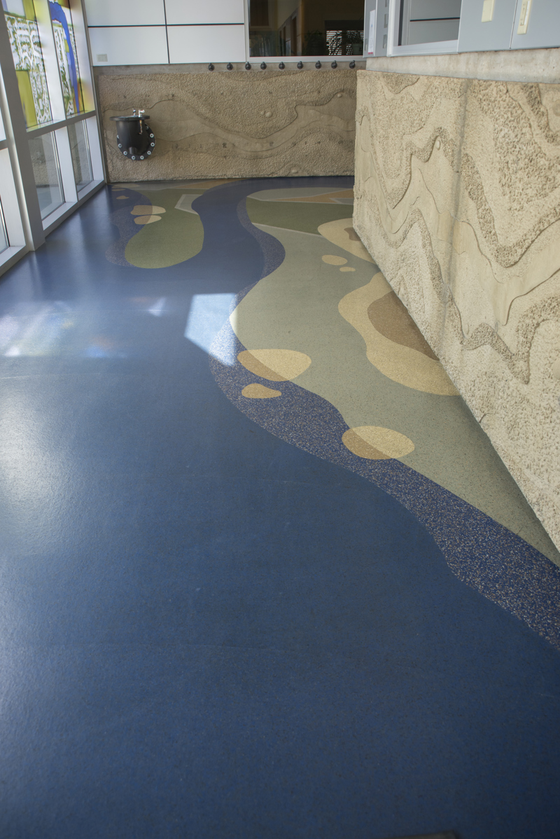 A terrazzo floor made to resemble a blue river meandering through a green landscape of green and yellow fields.