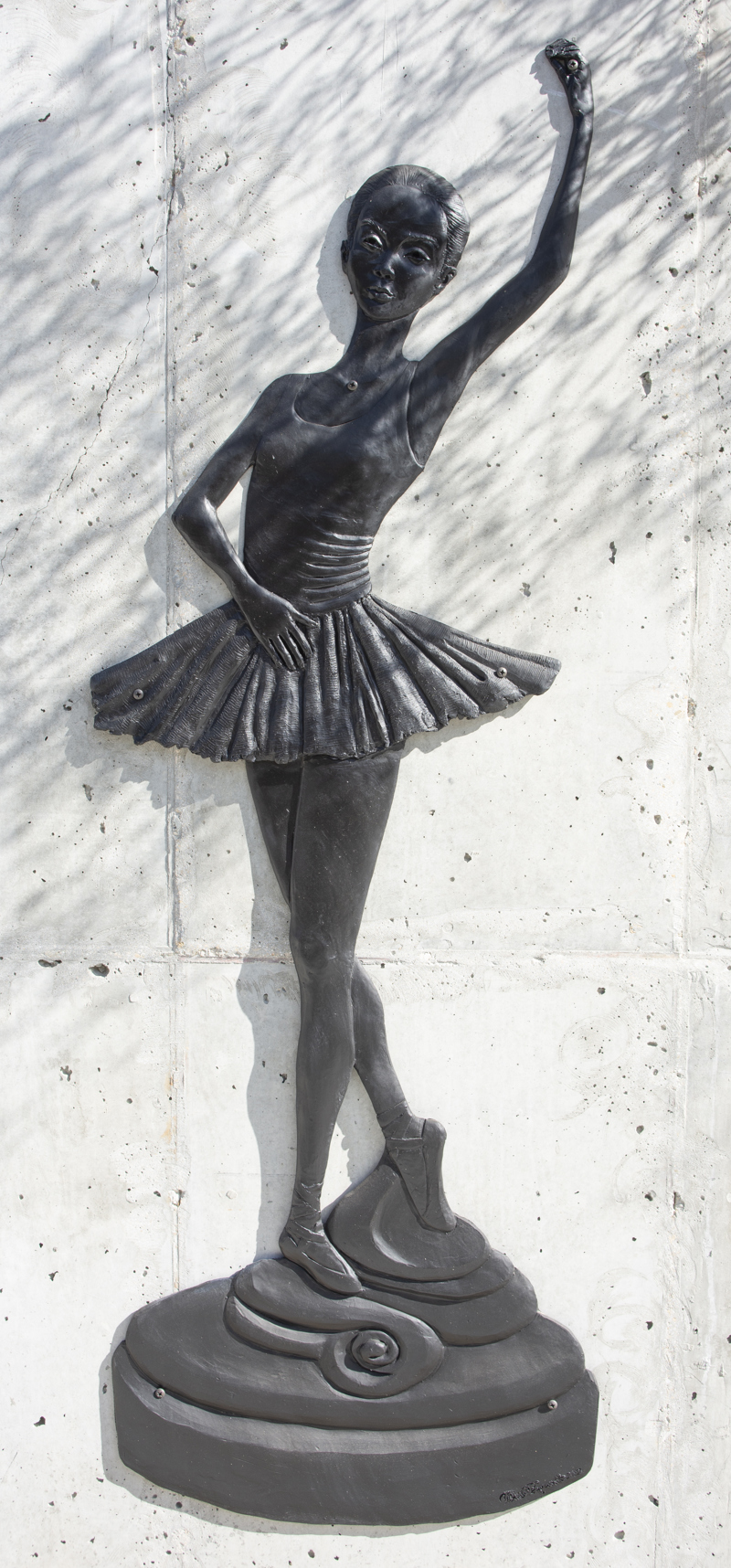 A low bas-relief bronze resin sculpture depicting a young ballerina standing on a pedestal.