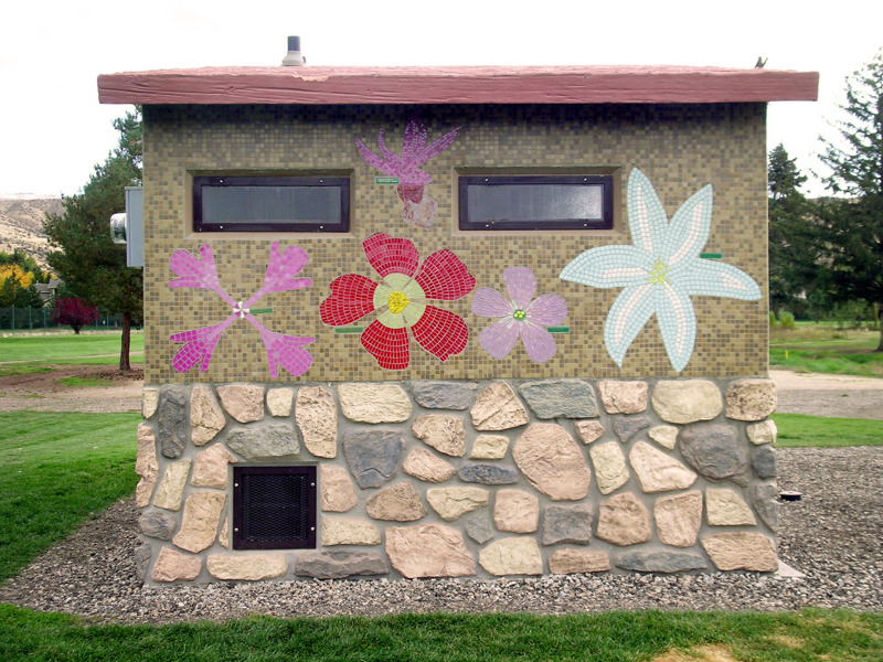 A small park bathroom building with sides covered in tile mosaics depicting flowers found in the state of Idaho. 