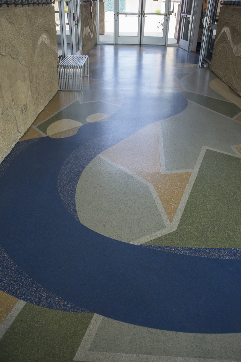 A terrazzo floor made to resemble a blue river meandering through a green landscape of green and yellow fields.