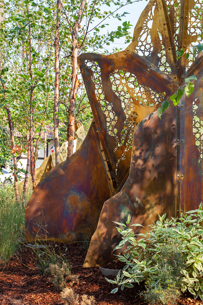 A geometric brass sculpture of mountain peaks topped with laser cut fabric patterns from various cultures. 