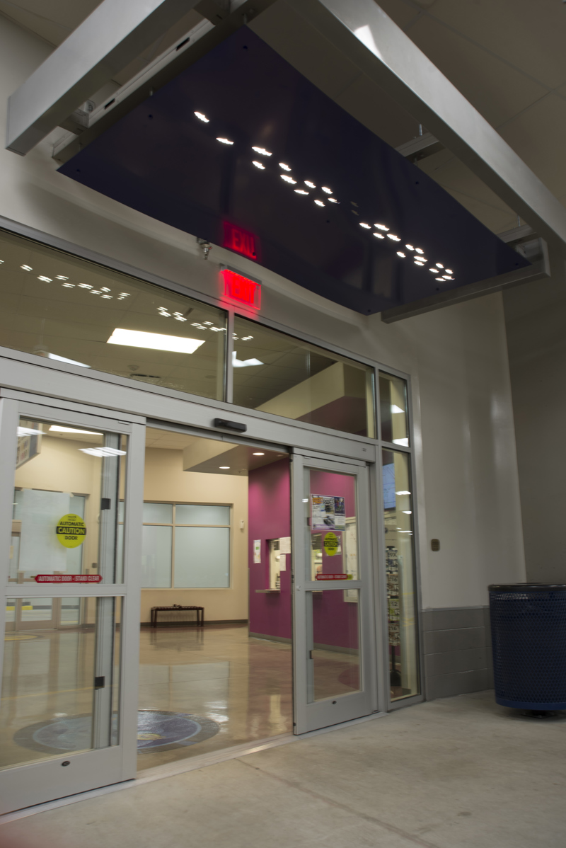 A doorway awning made of painted cut metal. In the awning, lit with backlighting, are holes in the shape of fish.