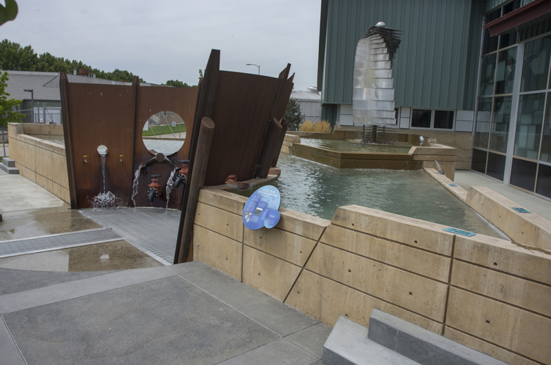 Fluxion is a sculpture that abuts a pool of water. The sculpture is made of 6 large curved plates of rusted industrial steel. In the plates are cut circular holes. Below the holes are several valve spickets of different sizes. Water from the pools spill through the holes and valves, and spills through a grate on the ground.