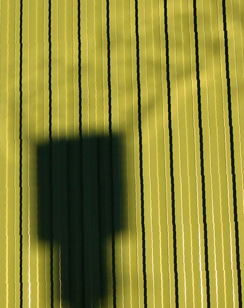 The shadow of a gas-burning chimney or methane flare stack against the green sheet siding of a building.