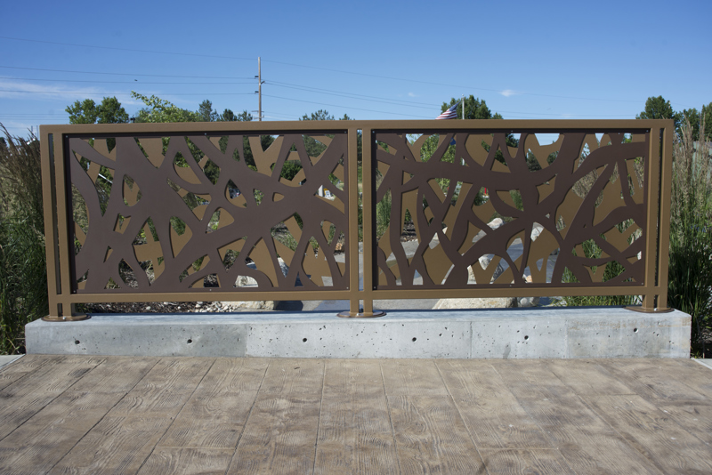 A safety railing made of two layers of brown-painted steel panels cut to resemble the tangled materials used in a beaver dam. 