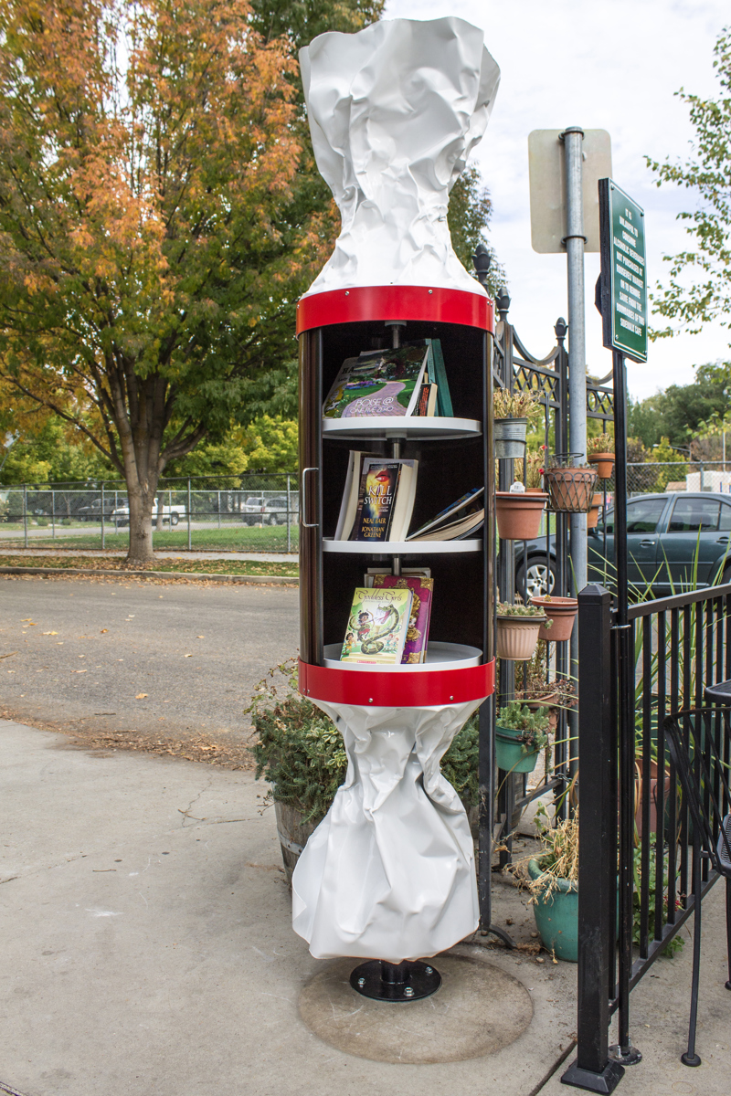 A little free library in the shape of a wrapped Tootsie Roll candy. In place of the usual wrapper text are the words "Free Brain Candy."
