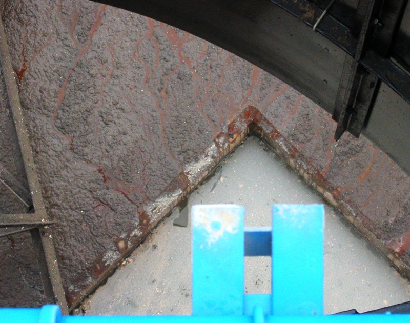 An industrial vat with dirty water and mud at its bottom. In the foreground is a bright blue pipe and bracket.