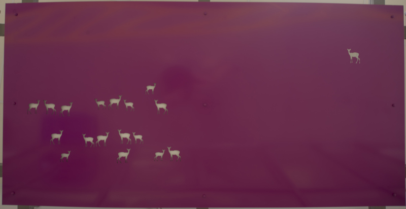 A doorway awning made of painted cut metal. In the awning, lit with backlighting, are holes in the shape of deer.