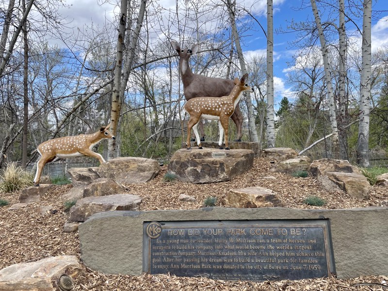 A painted sculpture of a deer and two fawns standing on a hill of rocks. Beneath them is a bronze plaque.