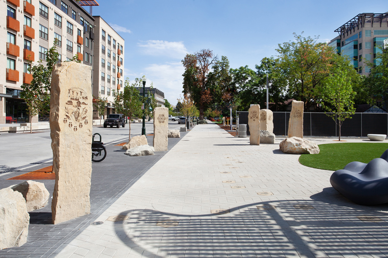 An image of five rough sandstone pillars with etchings representing different immigrant cultures. 