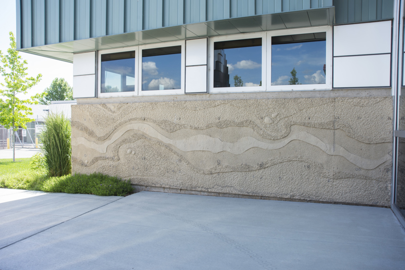The exterior back of the Boise WaterShed building. Along the bottom four feet of the building is a cement textural installation that resembles a birds-eye view or map of a river and its previous shorelines that have shifted over time.