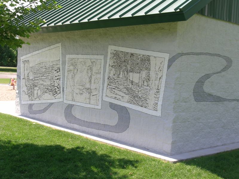 A park restroom shelter made of cinderblock. Painted on the outside is a mural depicting several photographs.