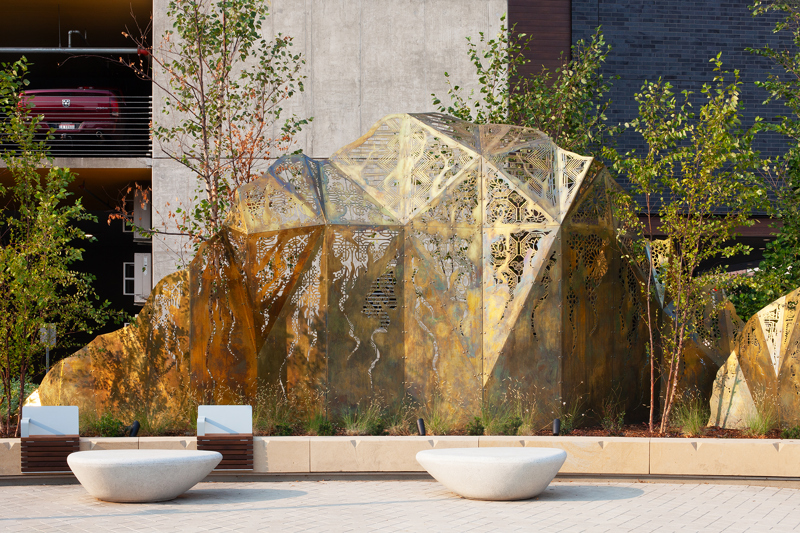 A geometric brass sculpture of mountain peaks topped with laser cut fabric patterns from various cultures. 