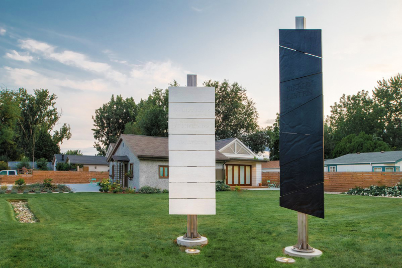Two standing sculptures made of cement panels affixed to steel poles. One sculpture appears white with the cement panels looking like 8 horizontal planks of wood with sunken text that reads, "When you look at something, really look." The other sculpture appears black with slanted cement panels that have the surface texture of flagstone with sunken text that reads, "Silent listen." 